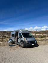 Scenic RV rental adventure: Silver campervan parked outdoors with snow-capped mountains and red rocks in the background.