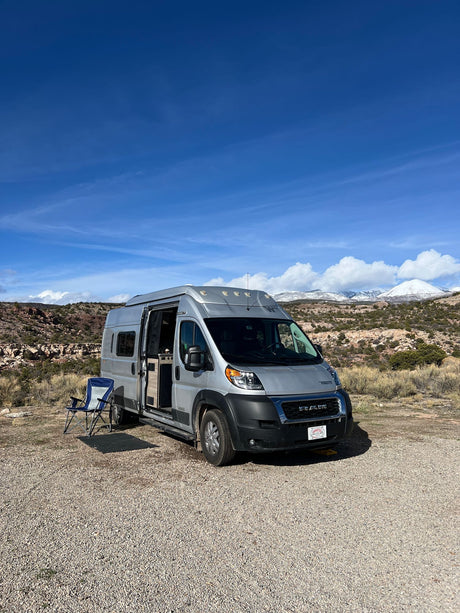 Scenic RV rental adventure: Silver campervan parked outdoors with snow-capped mountains and red rocks in the background.