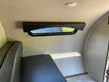 Inside an RV rental, showing a window with daylight, a ceiling light, and dark cushions forming a bed or bench area.