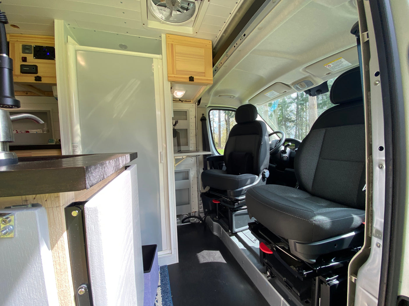 Step inside this RV rental, showcasing a camper van interior with a kitchen, swiveling front seats, and built-in amenities.