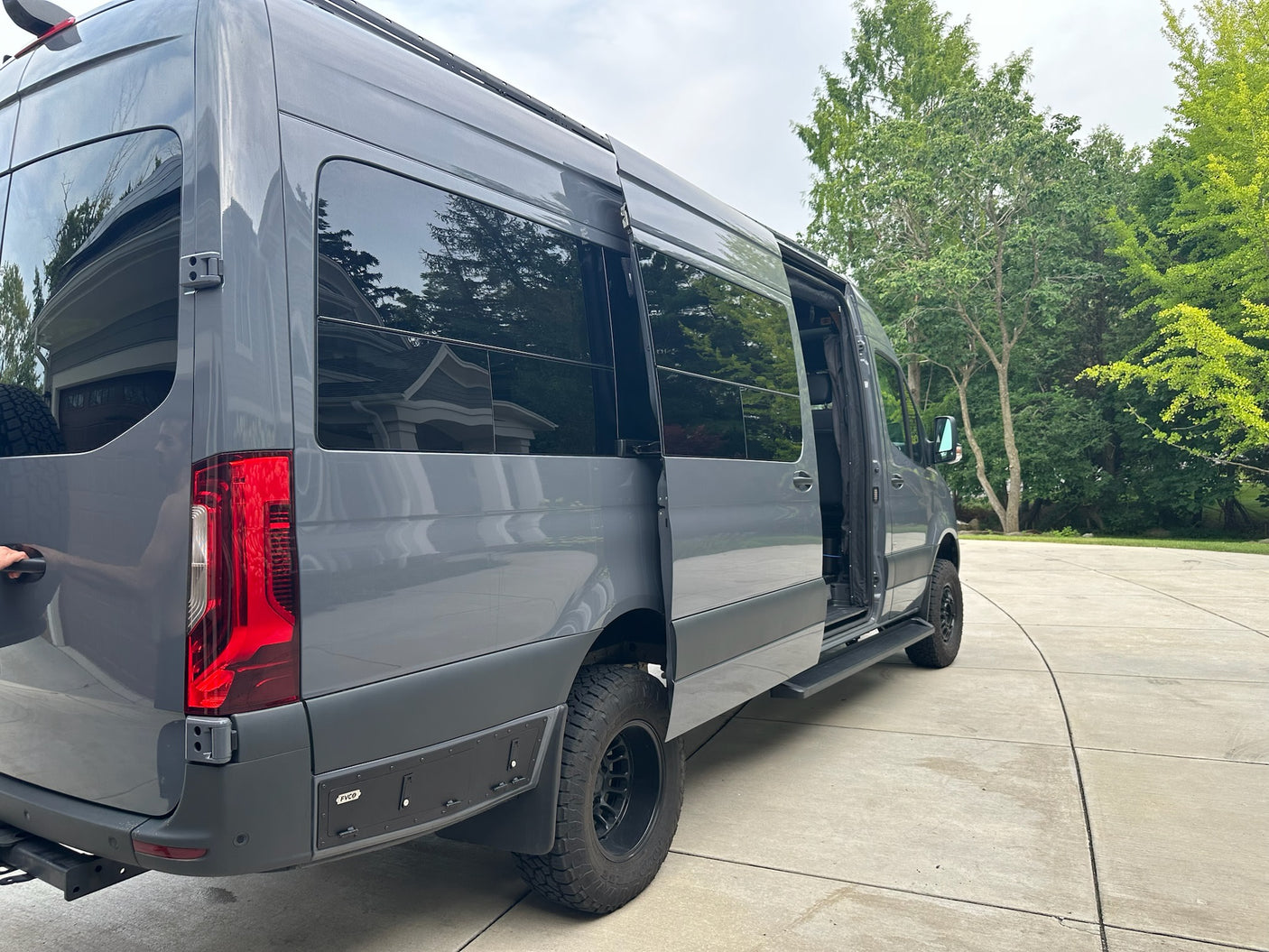 Gray custom camper van with an open side door, parked on a driveway. Ideal for your next rv rental adventure.
