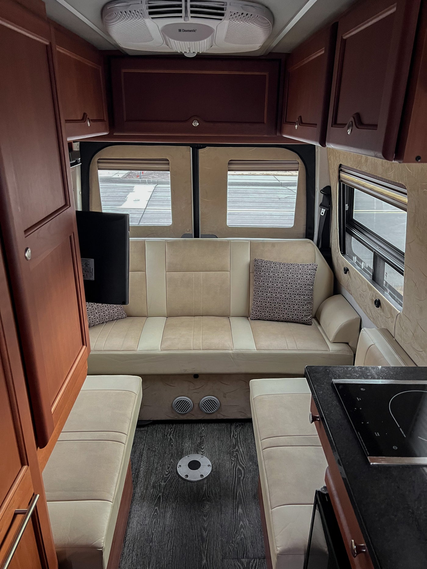 Inside a modern RV rental: comfortable cream seating, overhead storage, AC, TV, and a countertop with stove visible. — photo 18