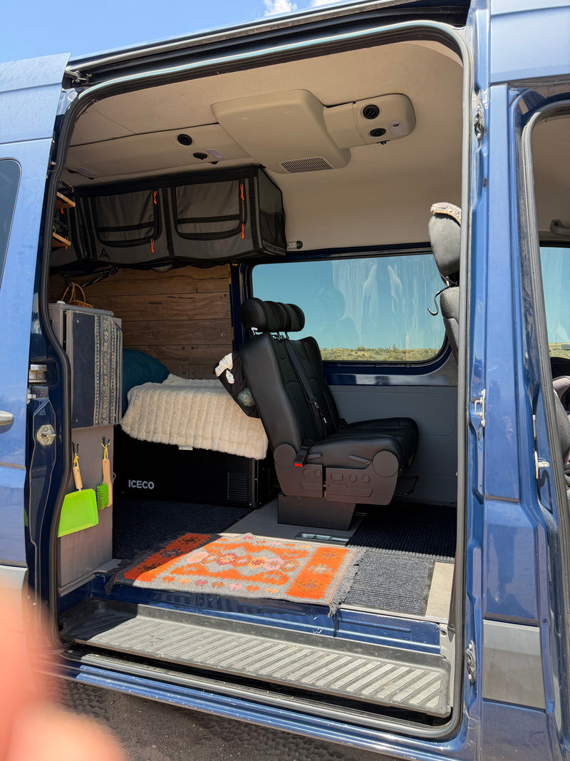 An rv rental camper van interior shows a bed, fridge, passenger seat, custom wood walls, and hanging storage bags. — photo 7