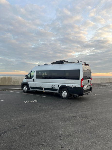 Silver Sequence camper van, ideal RV rental for oceanfront travel. Parked seaside at a cloudy sunrise/sunset.