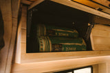 Organized overhead cabinet in an RV rental, featuring two green C.C. Filson blankets and warm wooden finishes.
