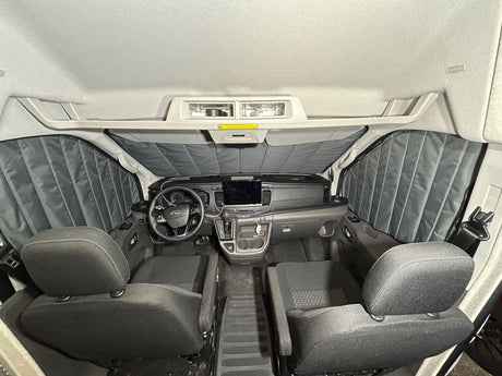 Inside an RV rental van: a clean front cabin with dashboard, steering wheel, two bucket seats, and quilted window coverings.