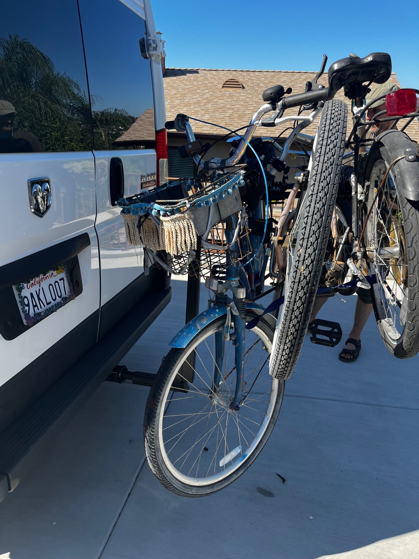 White Ram ProMaster RV rental with two bicycles on a rear rack. A person and California plate are visible.