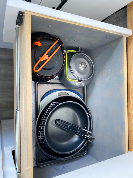 Compact cooking essentials, including pots, pans, and kettle, neatly stored in an RV rental drawer for easy access on your trip.