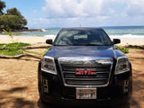Black GMC SUV parked on a sunny beach with ocean waves. An ideal vehicle for travel. Explore our RV rental options!