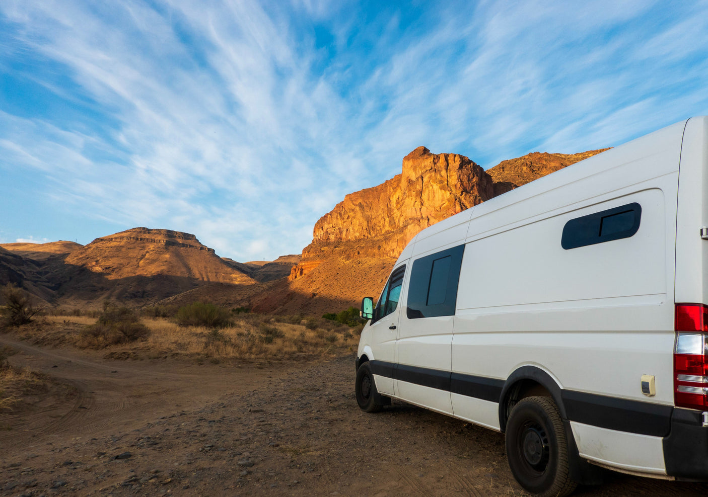 White rv rental camper van parked in a stunning, sun-drenched canyon landscape, inviting outdoor adventure.
