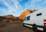 White rv rental camper van parked in a stunning, sun-drenched canyon landscape, inviting outdoor adventure.