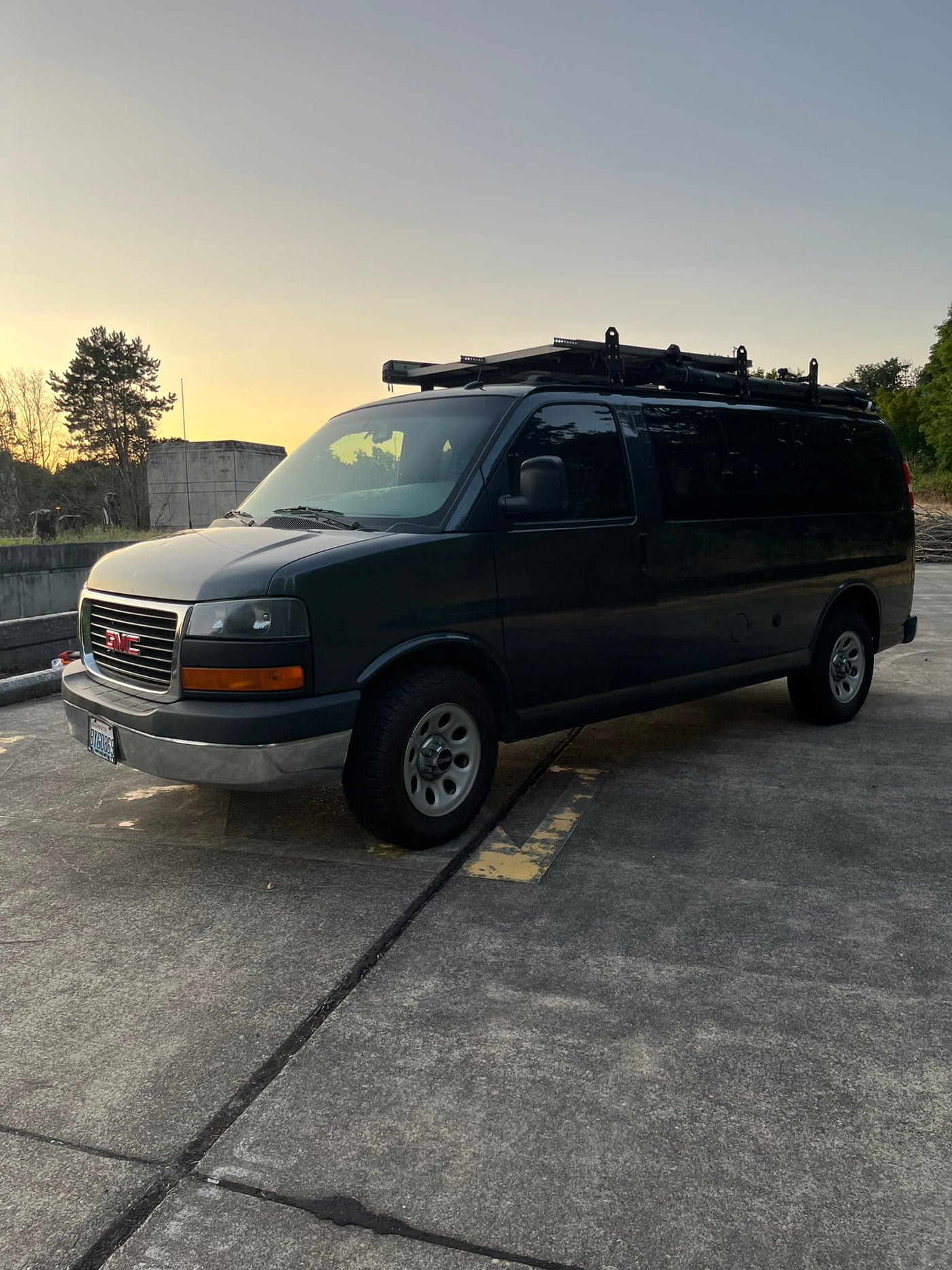 Dark GMC van with roof rack, ready for rv rental adventures. Parked on asphalt at dusk, ideal for your next road trip. — photo 12