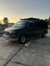 Dark GMC van with roof rack, ready for rv rental adventures. Parked on asphalt at dusk, ideal for your next road trip.