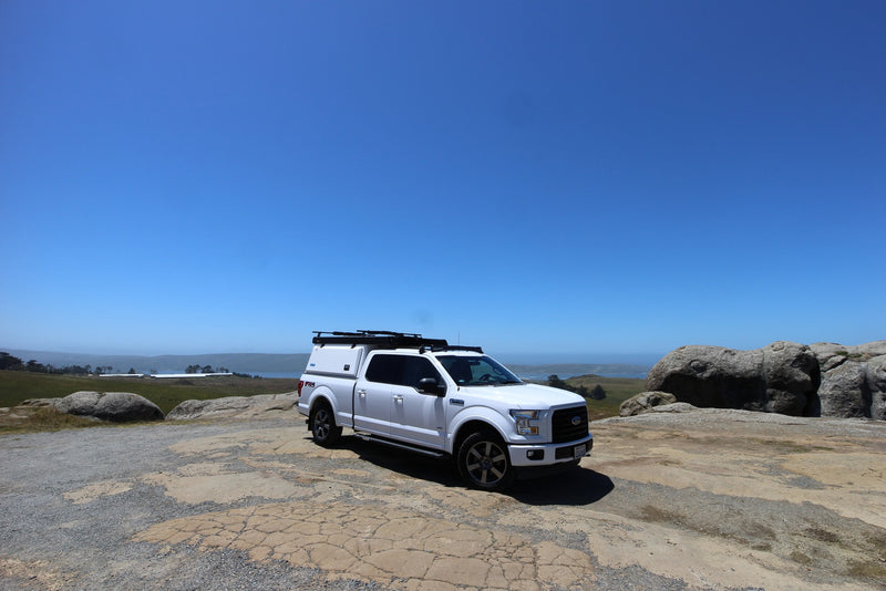 White Ford F-150 pickup with camper shell and roof rack, parked on a rocky overlook by the ocean. Ideal RV rental adventure. — photo 15