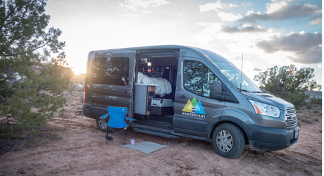 A grey Wandervans camper van RV rental is open for camping in a scenic desert landscape at sunset.