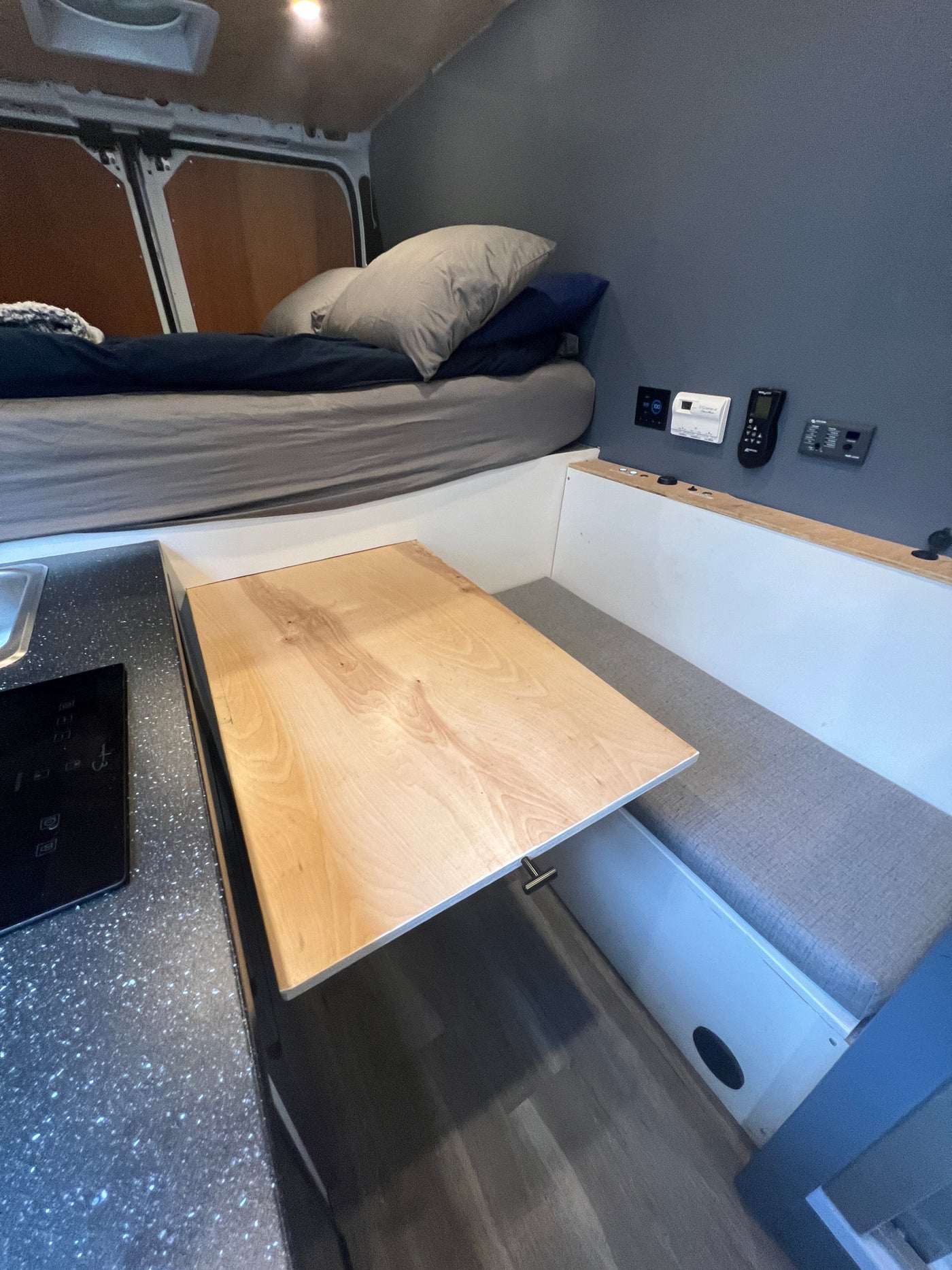 Compact RV rental interior featuring a bed, pull-out table with bench seating, and a small kitchen counter with a cooktop. — photo 4
