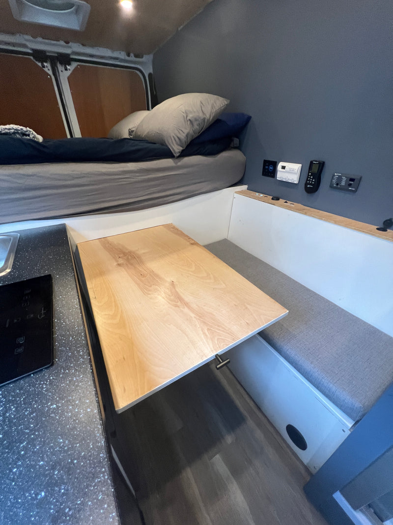 Compact RV rental interior featuring a bed, pull-out table with bench seating, and a small kitchen counter with a cooktop. — photo 4