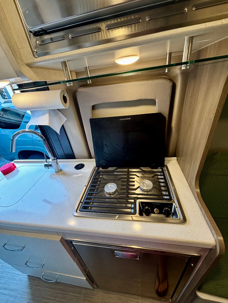 RV rental's compact kitchen setup: sink, two-burner Dometic stove, paper towels, and under-counter fridge.