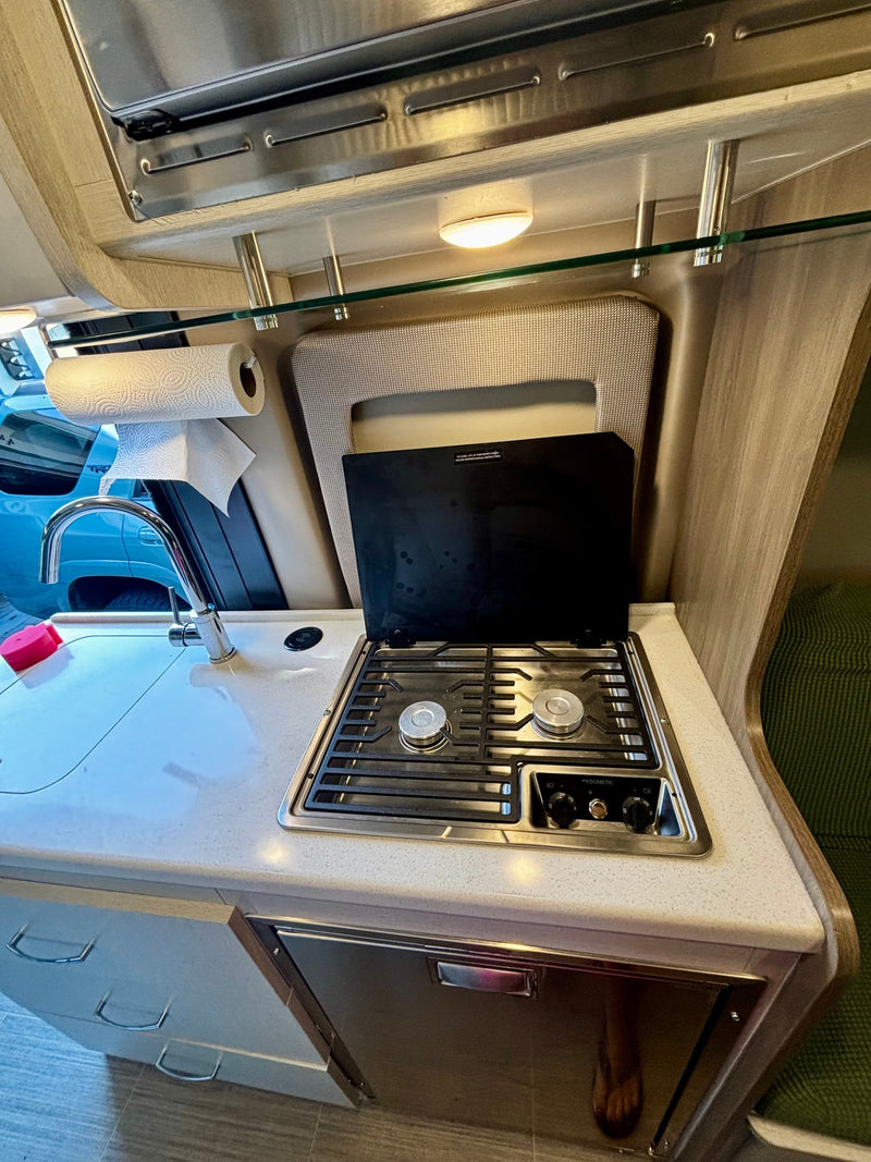 RV rental's compact kitchen setup: sink, two-burner Dometic stove, paper towels, and under-counter fridge. — photo 19