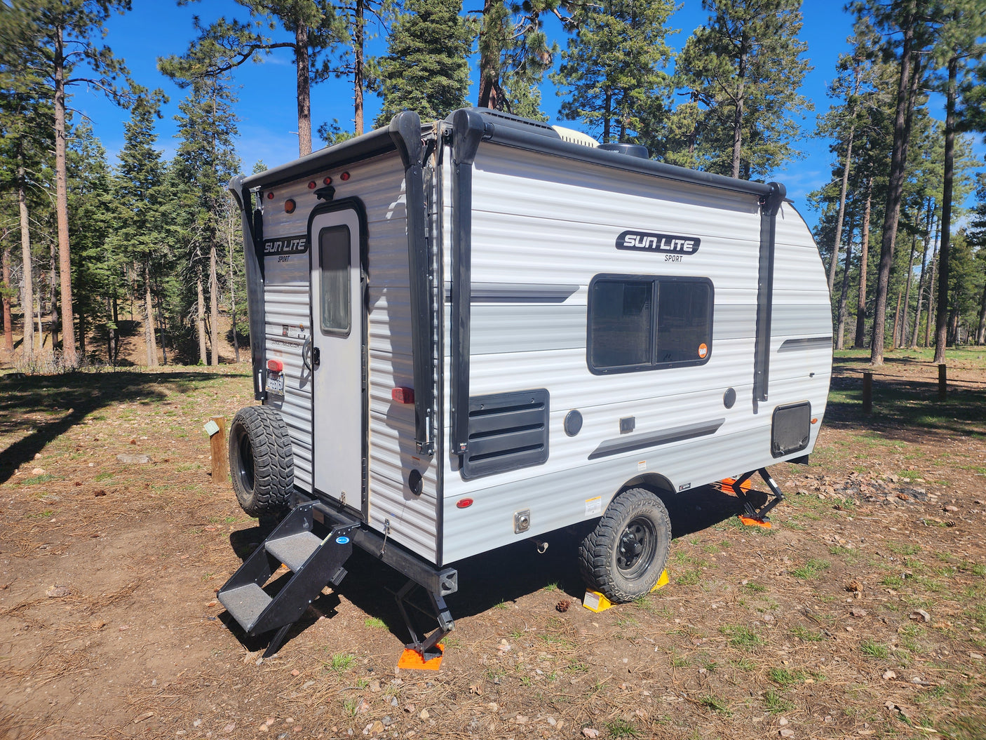Sun Lite Sport RV rental parked and leveled in a sunny pine forest campsite, ready for adventure.