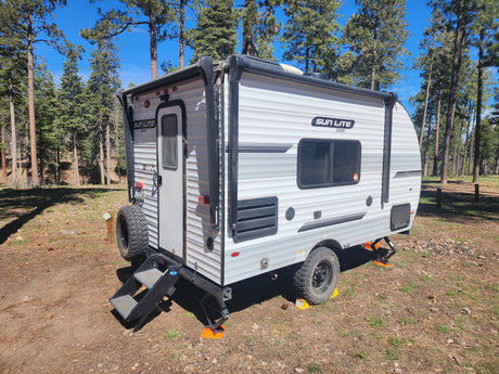 Sun Lite Sport RV rental parked and leveled in a sunny pine forest campsite, ready for adventure.