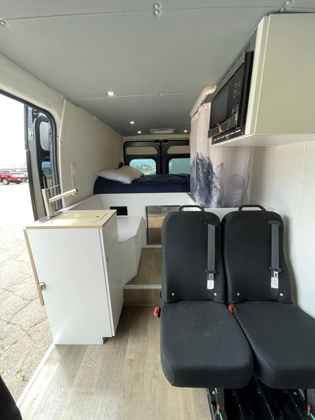 Inside an RV rental: A modern camper van interior with a bed, kitchenette, passenger seats, and microwave.