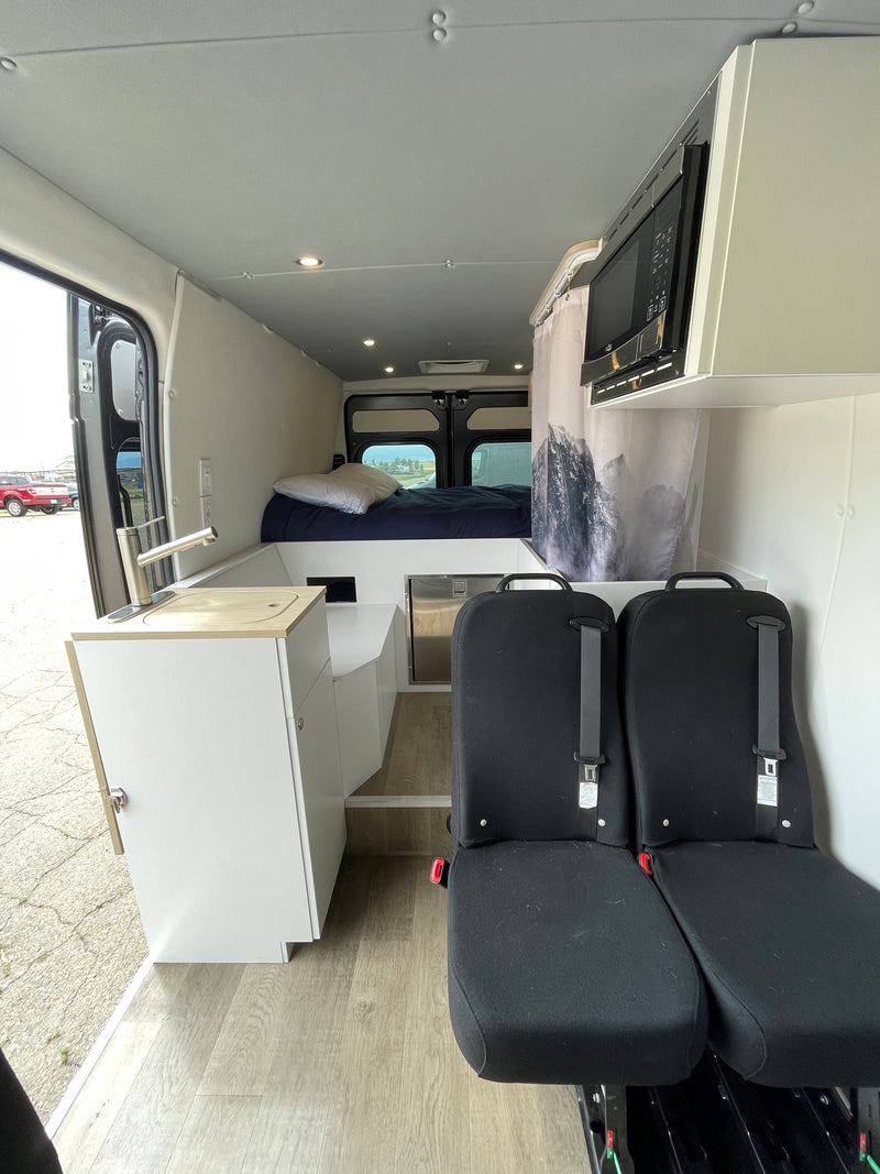 Inside an RV rental: A modern camper van interior with a bed, kitchenette, passenger seats, and microwave. — photo 6