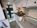 This modern RV rental interior features a functional compact kitchen, comfortable bench seating, and a built-in shower.