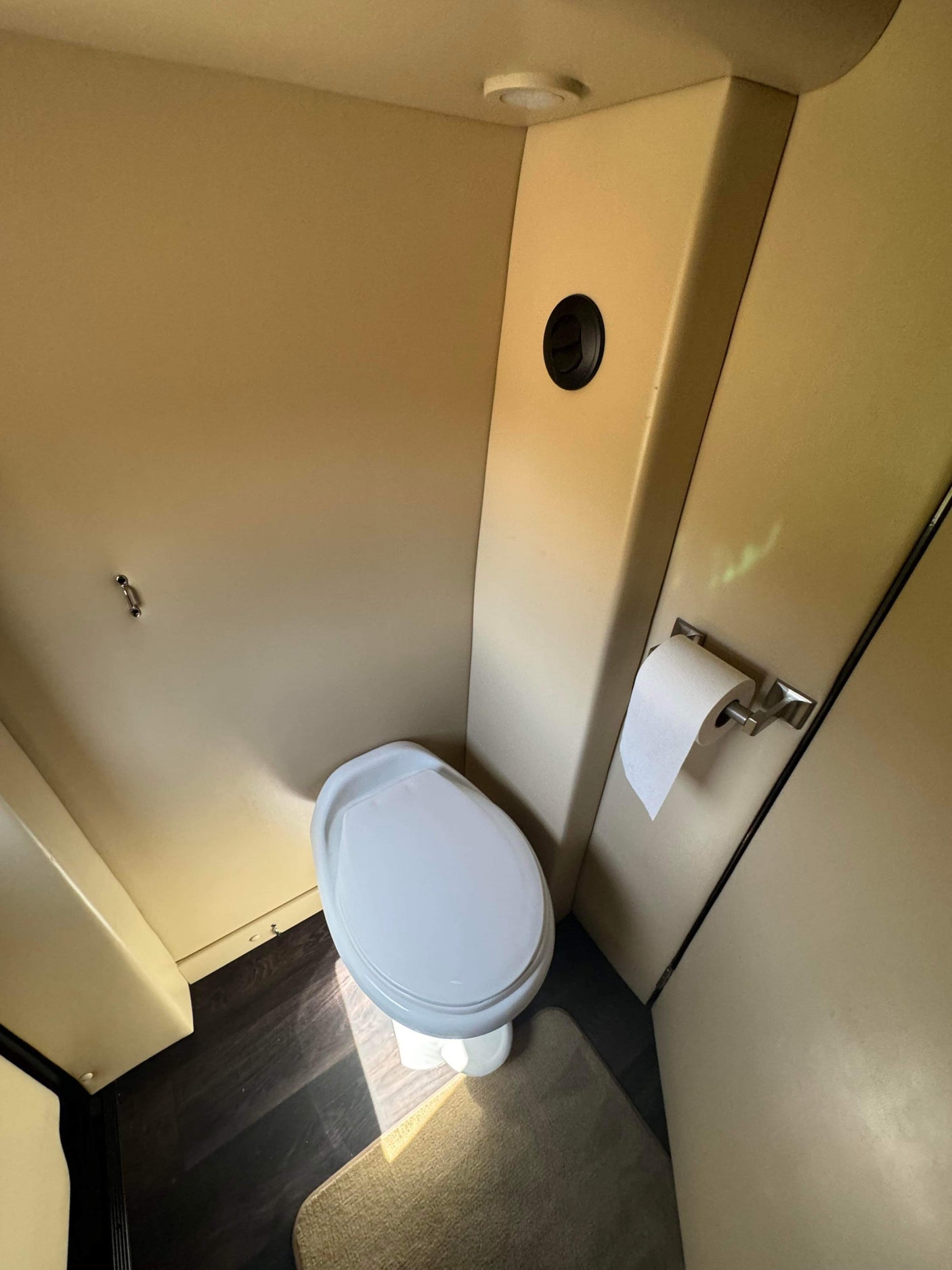 Inside an RV rental: a bright, compact bathroom featuring a white toilet, roll of toilet paper, and dark wood floor.