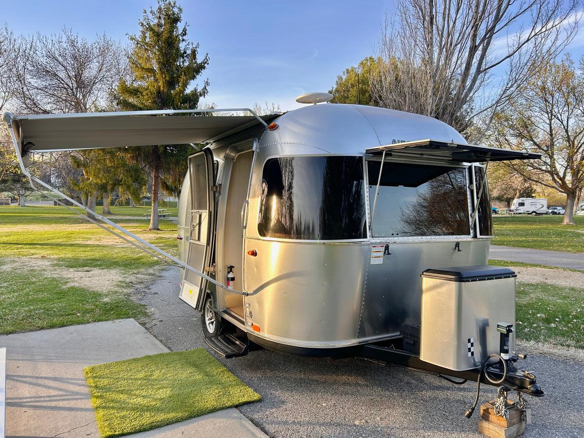 An Airstream RV rental is parked at a sunny campground with its awning extended and door open, ready for adventure.