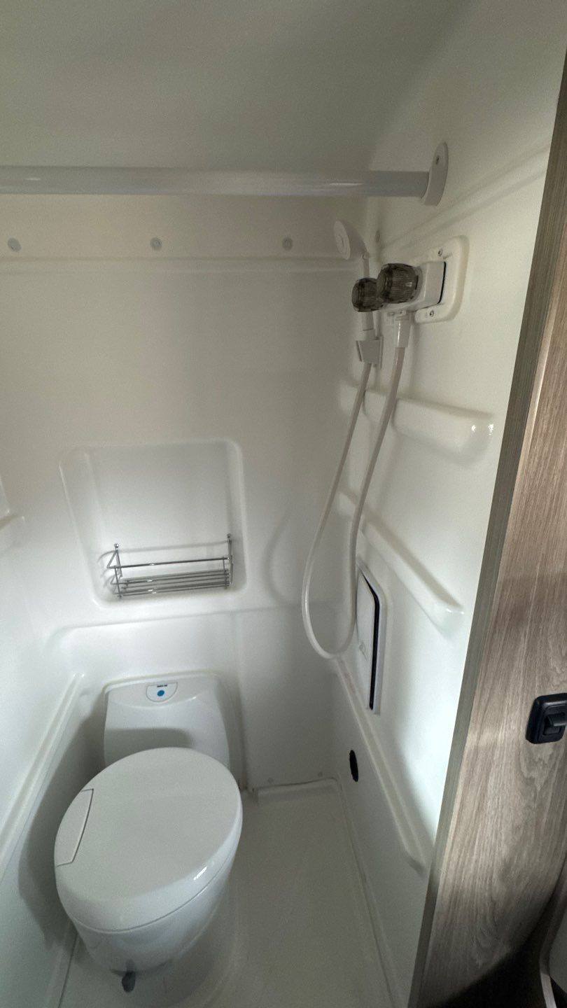 Clean, compact RV rental bathroom showing a toilet, handheld shower, and handy shelf for toiletries.