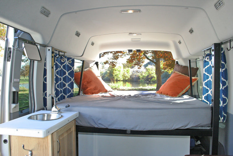 Inside a cozy RV rental: bed with scenic nature view, small sink, and blue curtains. Ideal for road trips and nature. — photo 2