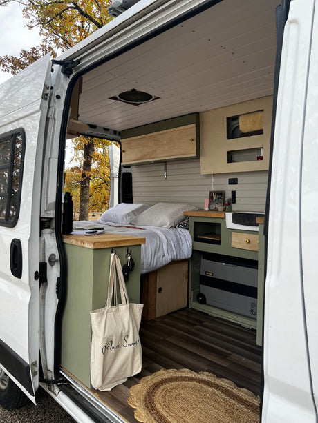  and rugged mountains under a clear blue sky.|View from an RV rental bed: cozy camper van with open back doors revealing a beautiful lake and autumn trees.|This cozy RV rental features a comfortable bed overlooking an autumn lake