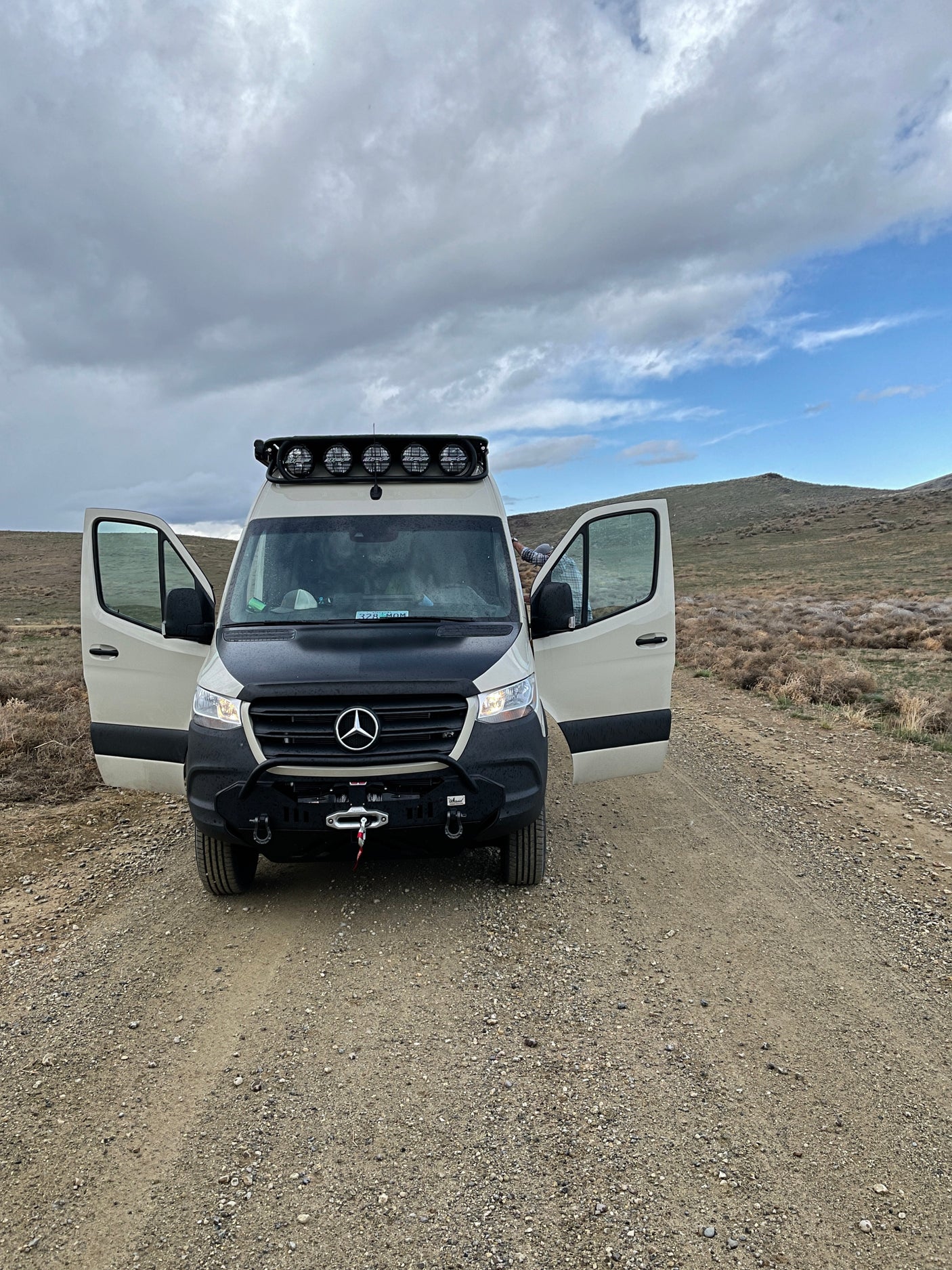 White Mercedes Sprinter RV rental with open doors, customized for adventure, parked on a dirt road in a vast landscape.