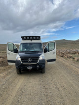 White Mercedes Sprinter RV rental with open doors, customized for adventure, parked on a dirt road in a vast landscape.