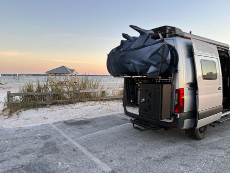 Enjoy beach travel with an RV rental! Camper van with outdoor gear parked by sandy shore and gazebo.