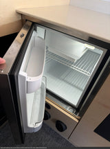 This RV rental features a clean, empty mini-fridge with wire shelves and door storage, illuminated and ready for use.