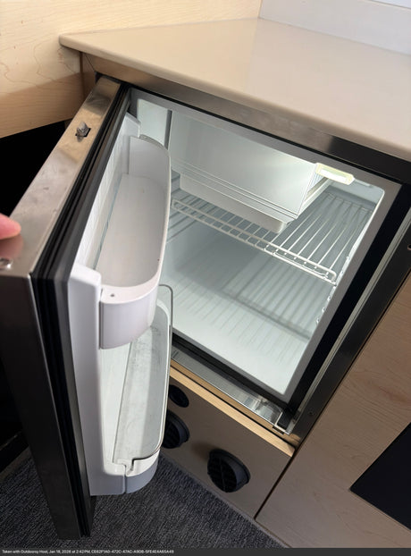This RV rental features a clean, empty mini-fridge with wire shelves and door storage, illuminated and ready for use.