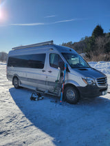 Silver RV rental van with skis & boots on snow, ready for a winter ski trip. Sunny day in the mountains.