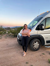 Smiling woman enjoys a beautiful desert sunset next to her Jayco RV rental camper van.