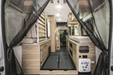 Spacious camper van rental interior from rear, showing beds, light wood cabinets, storage, and mesh screen.