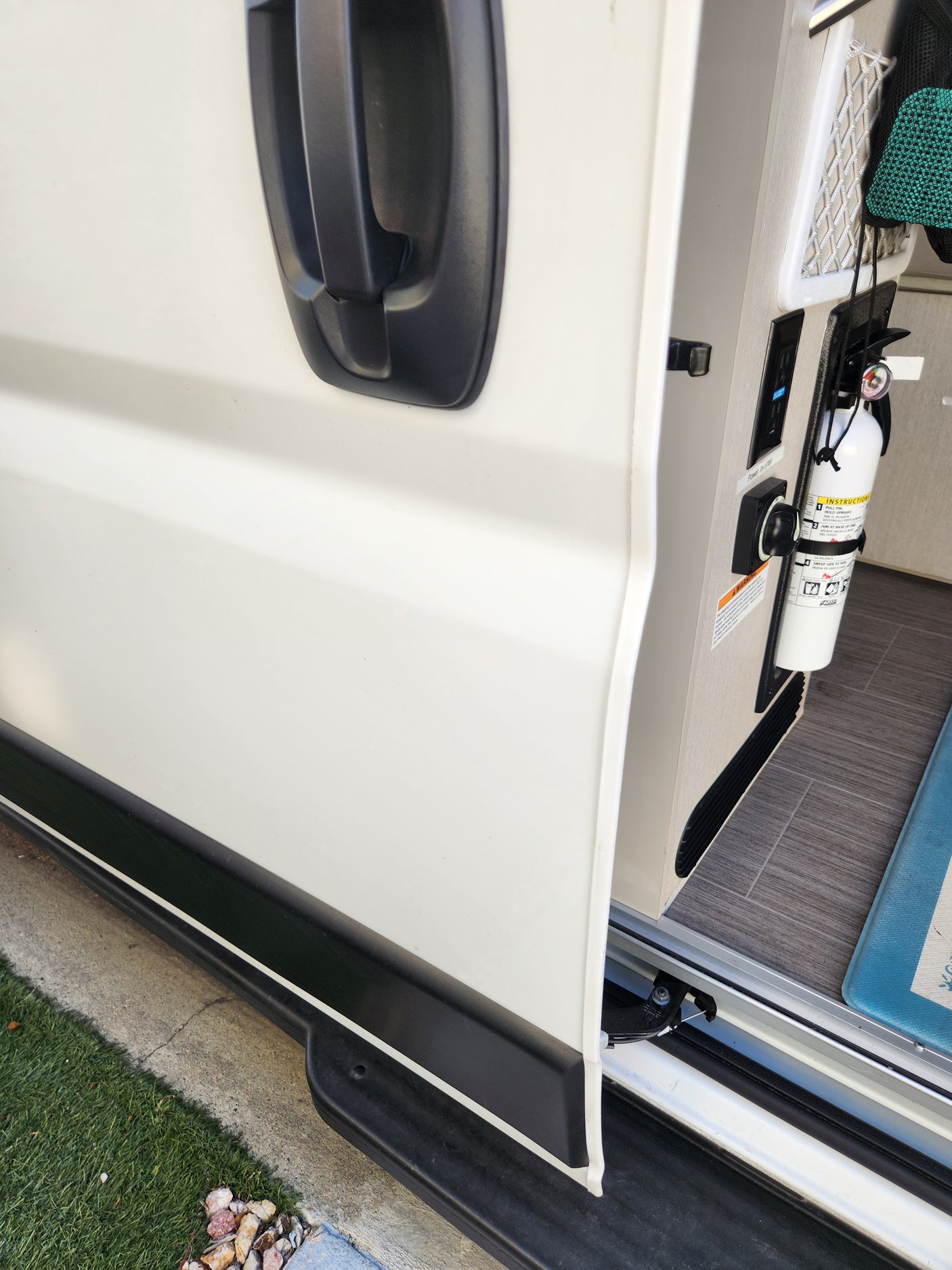RV rental side compartment open, revealing fire extinguisher, control panel, and storage net. A door handle is visible.