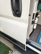 RV rental side compartment open, revealing fire extinguisher, control panel, and storage net. A door handle is visible.