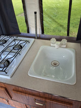 This RV rental's small kitchenette features a two-burner stove, sink, and wood cabinets, perfect for road trip cooking.