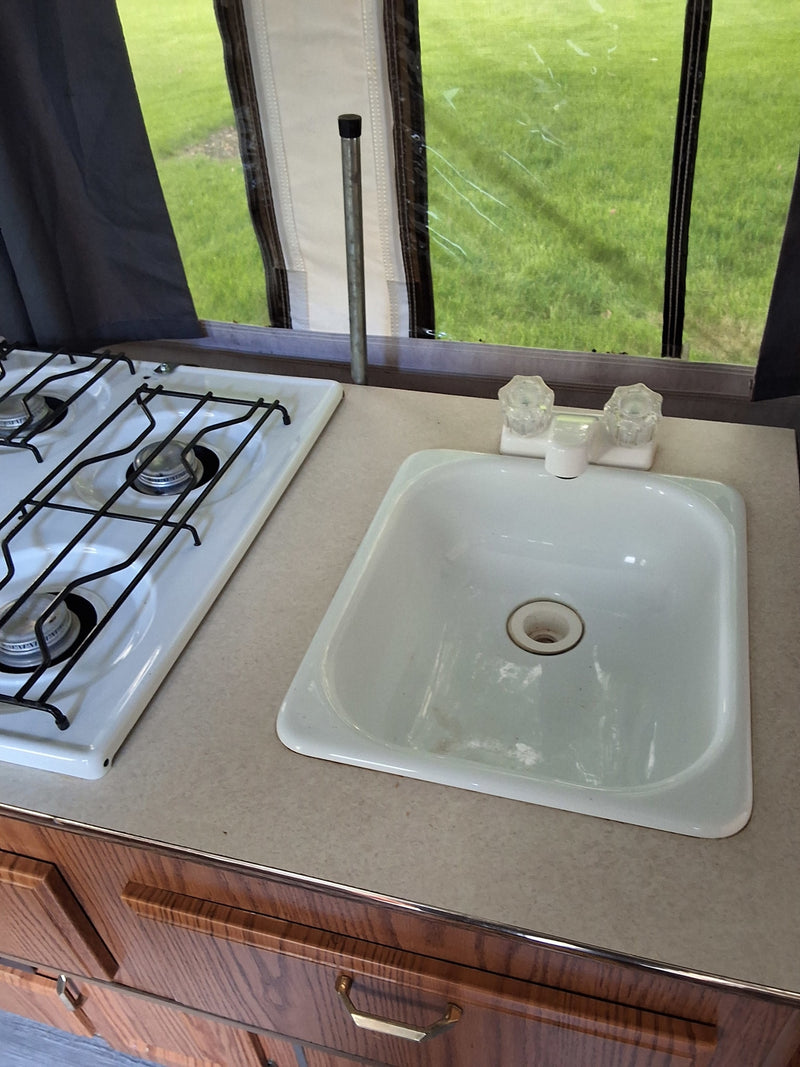This RV rental's small kitchenette features a two-burner stove, sink, and wood cabinets, perfect for road trip cooking. — photo 18