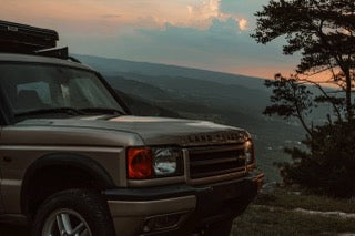 An overland Land Rover Discovery with a rooftop tent overlooks misty mountains at sunset, ready for your next rv rental adventure.