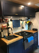 Functional & stylish RV rental kitchen. Features include navy cabinets, wood counters, black stove & sink, with organized spice racks.