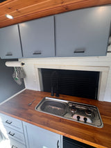 RV rental: Modern van kitchen features wood countertops, integrated sink/stove, gray cabinets, and a black faucet.