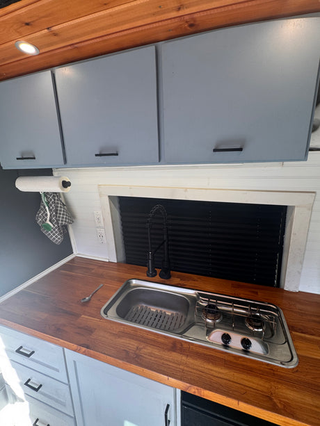 RV rental: Modern van kitchen features wood countertops, integrated sink/stove, gray cabinets, and a black faucet.