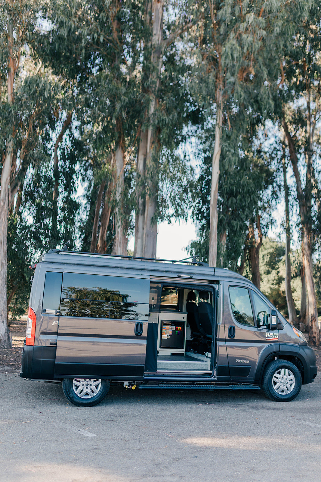 This grey Tofino camper van RV rental stands with its side door open, showcasing a functional interior setup for road trips.